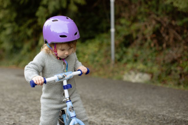 Smiling toddler riding an eco-friendly balance bike in a park with helmet on